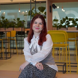 Unsere Auszubildende Laura sitzt im Social Space und lächelt in die Kamera