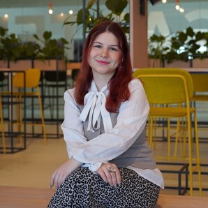 Unsere Auszubildende Laura sitzt im Social Space und lächelt in die Kamera
