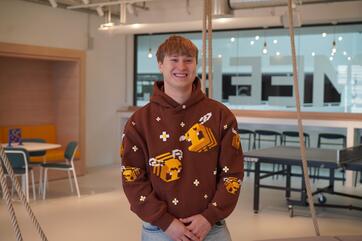 Unser Auszubildender Max sitzt im Social Space und lächelt in die Kamera