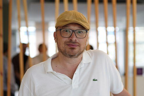 Alexander Mannsfeld AlMa Techblog Autor Das Bild zeigt den Techblog-Autor Alexander Mannsfeld mit weißem Poloshirt und Schiebermütze in einem Social Space des OTTO-Gebäudes