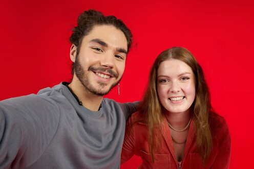 Zwei Kollegen umarmen sich Zwei Kollegen von OTTO umarmen sich lächelnd und stehen vor einem roten Hintergrund.