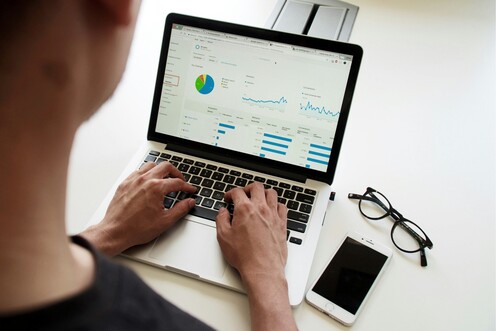 Eine Person arbeitet am Laptop. Neben dem Laptop liegen Handy und Brille.