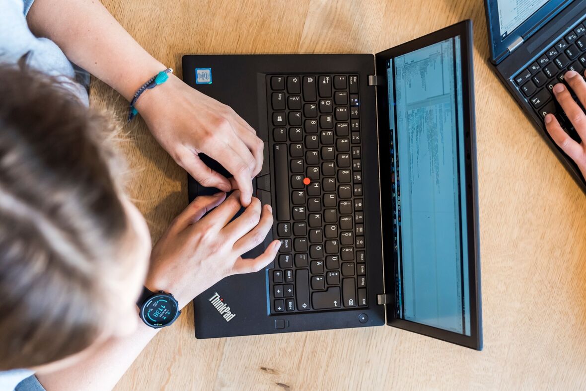 Zwei Kollegen sitzen sich mit ihren Laptopen gegenüber und tippen darauf.
