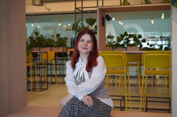 Unsere Auszubildende Laura sitzt im Social Space und lächelt in die Kamera