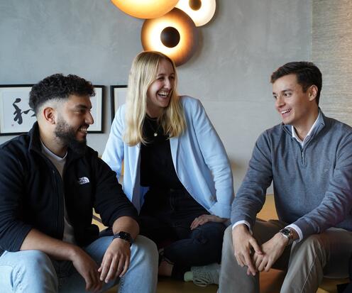 Drei Azubis sitzen zusammen auf dem Sofa reden und lachen gemeinsam.