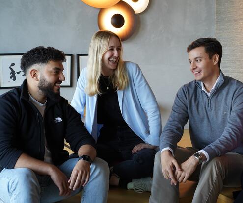 Azubis im Austausch Drei Azubis sitzen zusammen auf dem Sofa reden und lachen gemeinsam.