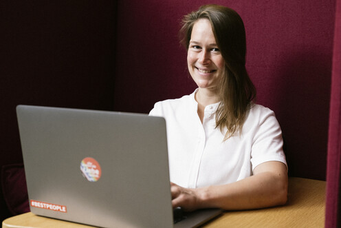 Unsere Kollegin aus Data Scientist sitzt am Laptop Kollegin aus Data Scientist sitzt lächelnd am Laptop in einer gemütlichen, gepolsterten Ecke bei OTTO