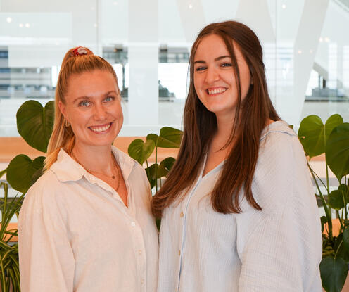 Unsere Recruiterinnen im Social Space Zwei Rekrutinnen aus einem Team stehen lächelnd vertraut im Social Space