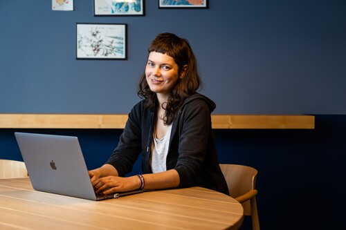 Unsere Kollegin bei der Arbeit als Softwareentwicklerin Softwareentwicklerin sitzt mit Laptop am Tisch und lächelt in die Kamera