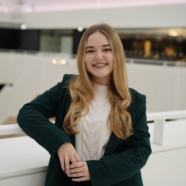 Unsere Junior HR-Managerin lächelt in die Kamera Unsere Kollegin ist Junior HR-Managerin im PM-Team. Sie lehnt sich mit dem Arm am Geländer ab und lächelt in die Kamera. Sie befindet sich im Headquarter Gebäude von OTTO.