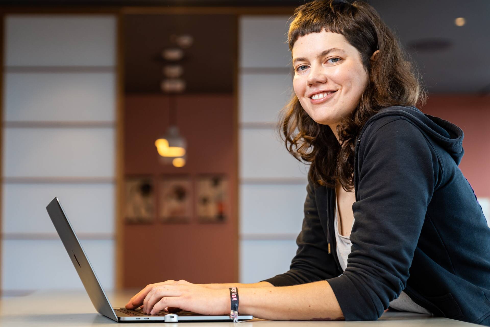 Softwareentwicklerin sitzt am Computer und guckt freundlich zur Seite in die Kamera.