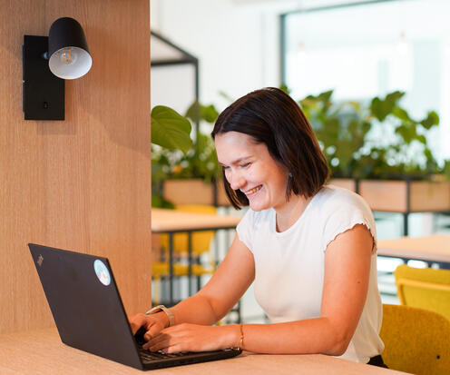 Checkliste Bewerbung Kein Anschreiben nötig Das Bild zeigt eine junge Frau am modernen und freundlichen Otto Campus, die grinsend ihr Notebook bedient. Das Bild symbolisiert, dass für Bewerbungen bei OTTO kein Anschreiben nötig ist.