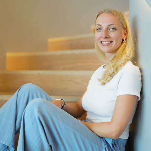 Unsere Praktikantin sitzt auf der Treppe Eine Praktikantin sitzt auf einer Treppenstufe und lehnt sich an und lächelt in die Kamera.