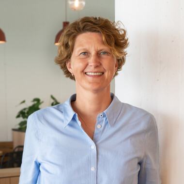 Führungskraft im Bereich Unternehmensstrategie steht im Social Space hat die Hände in der Hose und lächelt in die Kamera