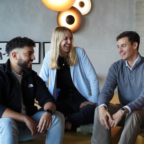 Azubis im Austausch Drei Azubis sitzen zusammen auf dem Sofa reden und lachen gemeinsam.