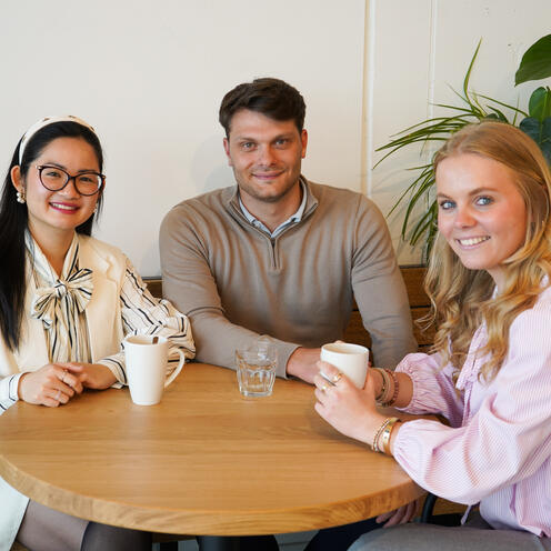 Drei unserer Werkstudent*innen sind beim Kaffeetrinken im Social Space auf dem Campus