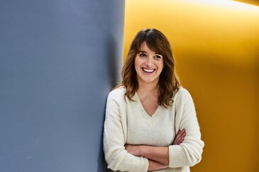 Unsere Kollegin lehnt sich an eine Wand und lächelt zur Seite.
