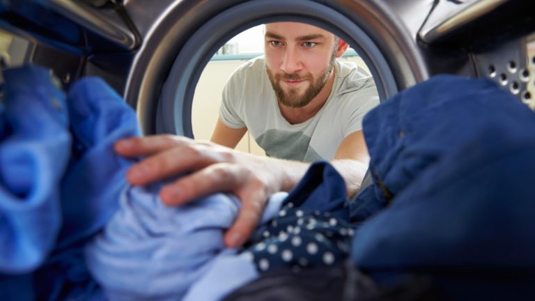 Mann gibt verschiedene blaue Kleidungsstücke in die Waschtrommel