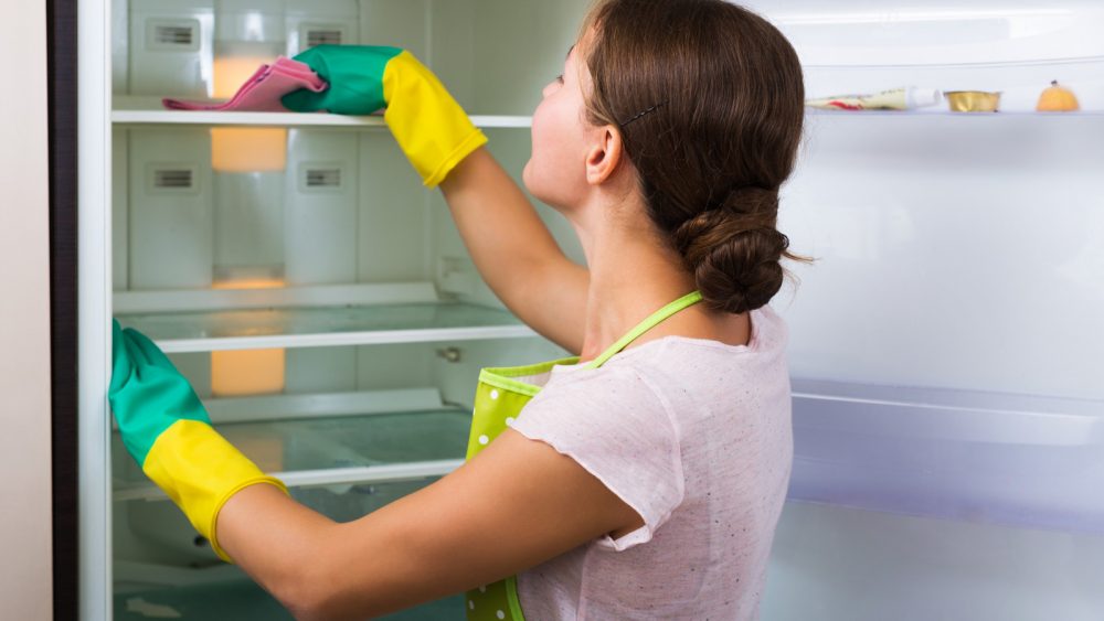 Frau wischt Tiefkühlfach des Kühlschranks aus