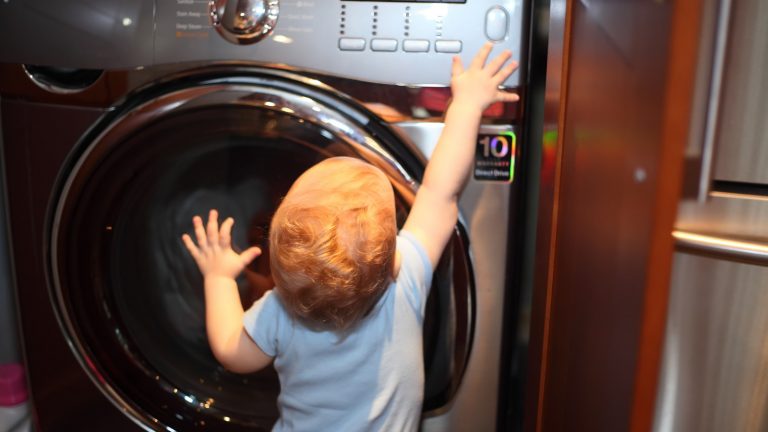 Kleinkind spielt an Knöpfen der Waschmaschine