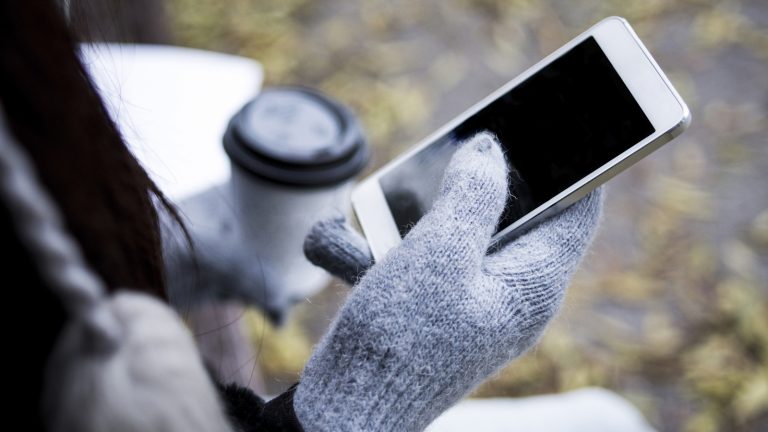 Eine Person mit Handschuhen hält ein Smartphone in der Hand.