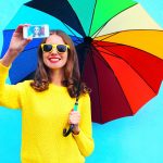 M&auml;dchen mit Sonnenbrille und Regenschirm macht Selfie