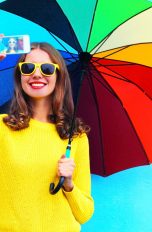Mädchen mit Sonnenbrille und Regenschirm macht Selfie
