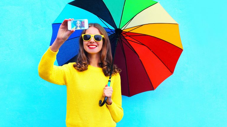 Mädchen mit Sonnenbrille und Regenschirm macht Selfie