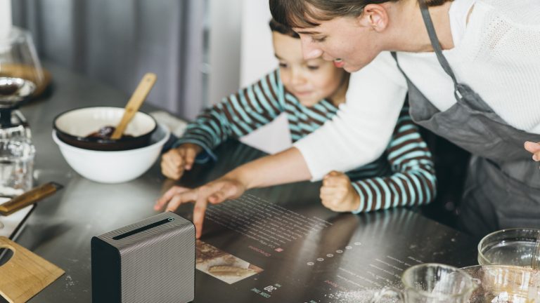 Mutter und Tochter beim Kochen mit projizierter Kochanleitung auf der Arbeitsfläche