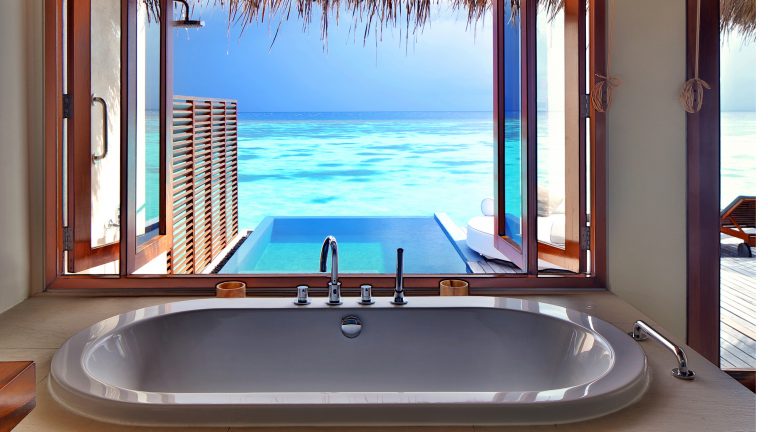 Badewanne vor einem großen Fenster mit Blick auf Pool und Meer