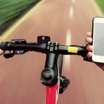 Fahrradfahrer st&uuml;tzt Hand auf Lenker, um Smartphone zu bedienen.