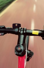 Smarte Jeansjacke Fahrradfahrer stützt Hand auf Lenker, um Smartphone zu bedienen.