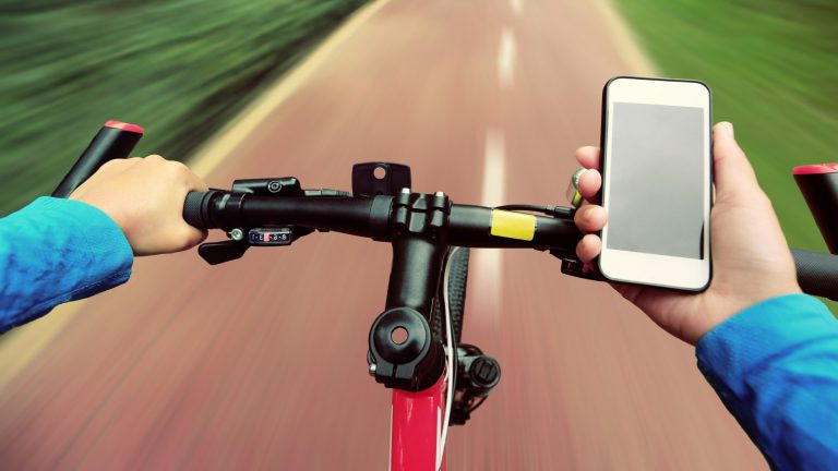 Fahrradfahrer stützt Hand auf Lenker, um Smartphone zu bedienen.