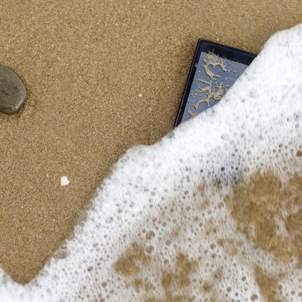 Smartphone am Strand wird vom Meerwasser verdeckt