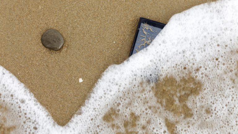 Smartphone am Strand wird vom Meerwasser verdeckt