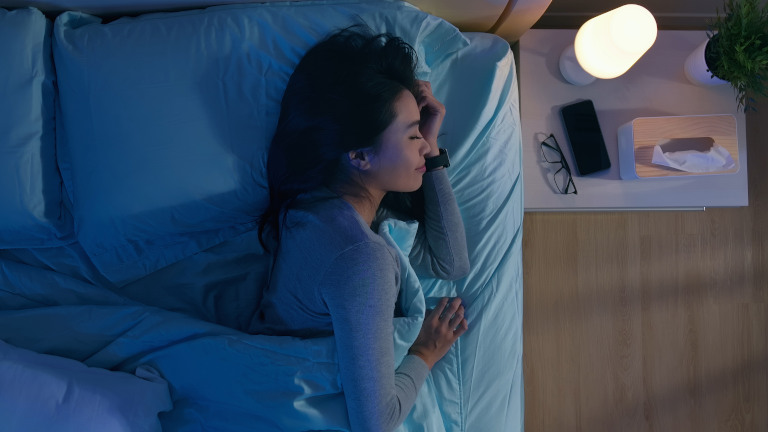 Frau im Bett mit iPhone im Nicht-stören-Modus auf dem Nachttisch