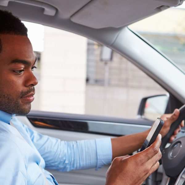 Ein Autofahrer bedient eine App auf seinem Smartphone.