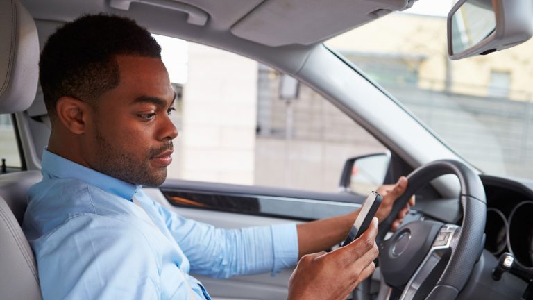 Ein Autofahrer bedient eine App auf seinem Smartphone.
