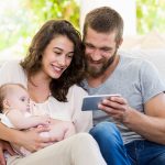 Eltern mit Kleinkind und Smartphone auf einem Sofa