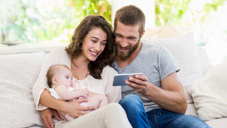 Eltern mit Kleinkind und Smartphone auf einem Sofa