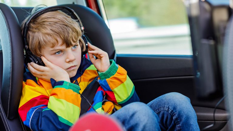 Kind schaut einen Film mit Kopfhörern auf dem Kindersitz des Autos