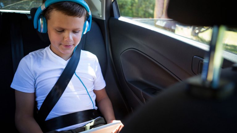 Kind mit Kopfhörern am Tablet im Auto