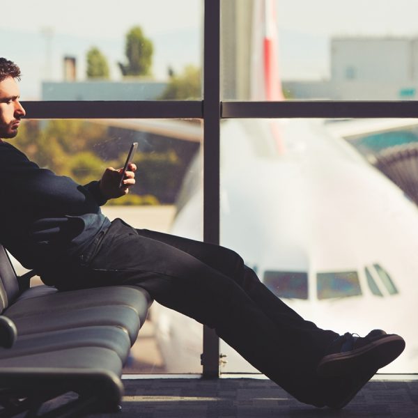 Ein Mann mit B&uuml;gel-Kopfh&ouml;rern sitzt am Terminal auf den Sitzen und schaut aufs Smartphone