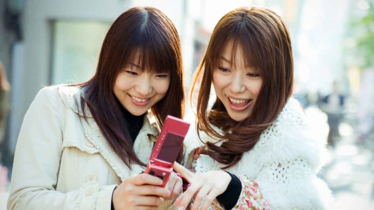Zwei weibliche Personen schauen gemeinsam auf ein rotes Klapptelefon