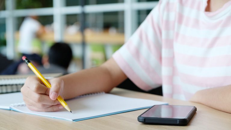 Schüler macht sich handschriftliche Notizen und nutzt das Smartphone