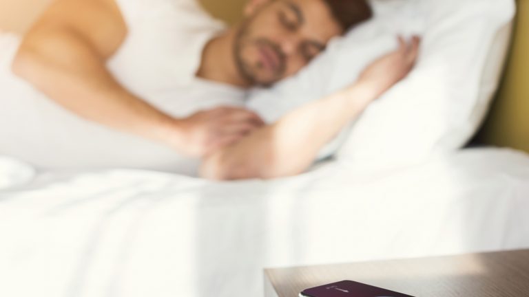 Smartphone liegt auf dem Nachtisch und überwacht den Schlaf eines Mannes