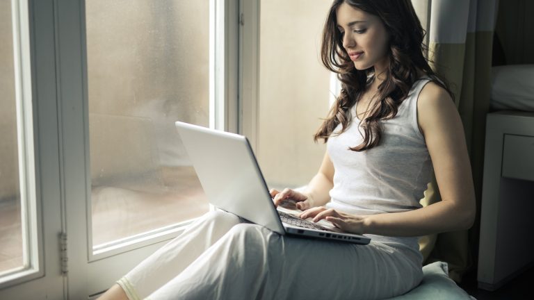 Frau am Fenster sitzend surft am Notebook