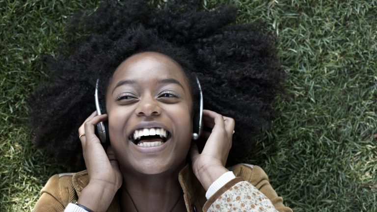 Junge Frau liegt im Gras und hört Musik über Kopfhörer