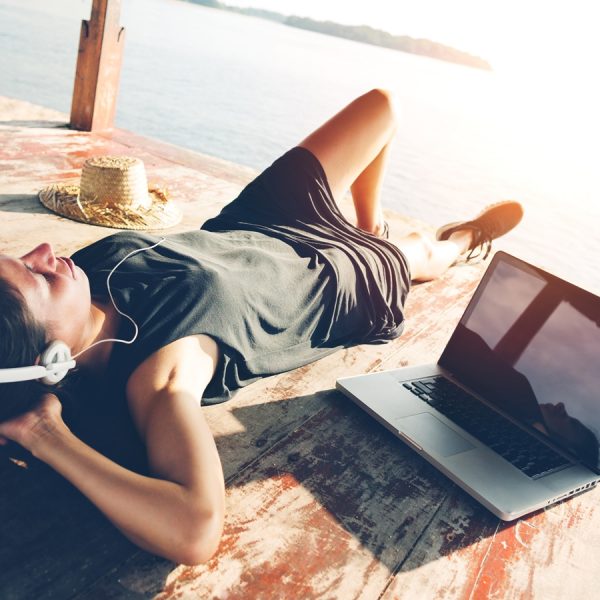 Junge Frau liegt am See und h&ouml;rt ihre Spotify-Playlist &uuml;ber ein Notebook
