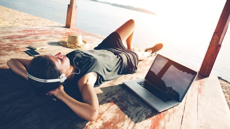 Junge Frau liegt am See und hört ihre Spotify-Playlist über ein Notebook